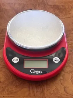 A red digital scale with a bowl on top of it.